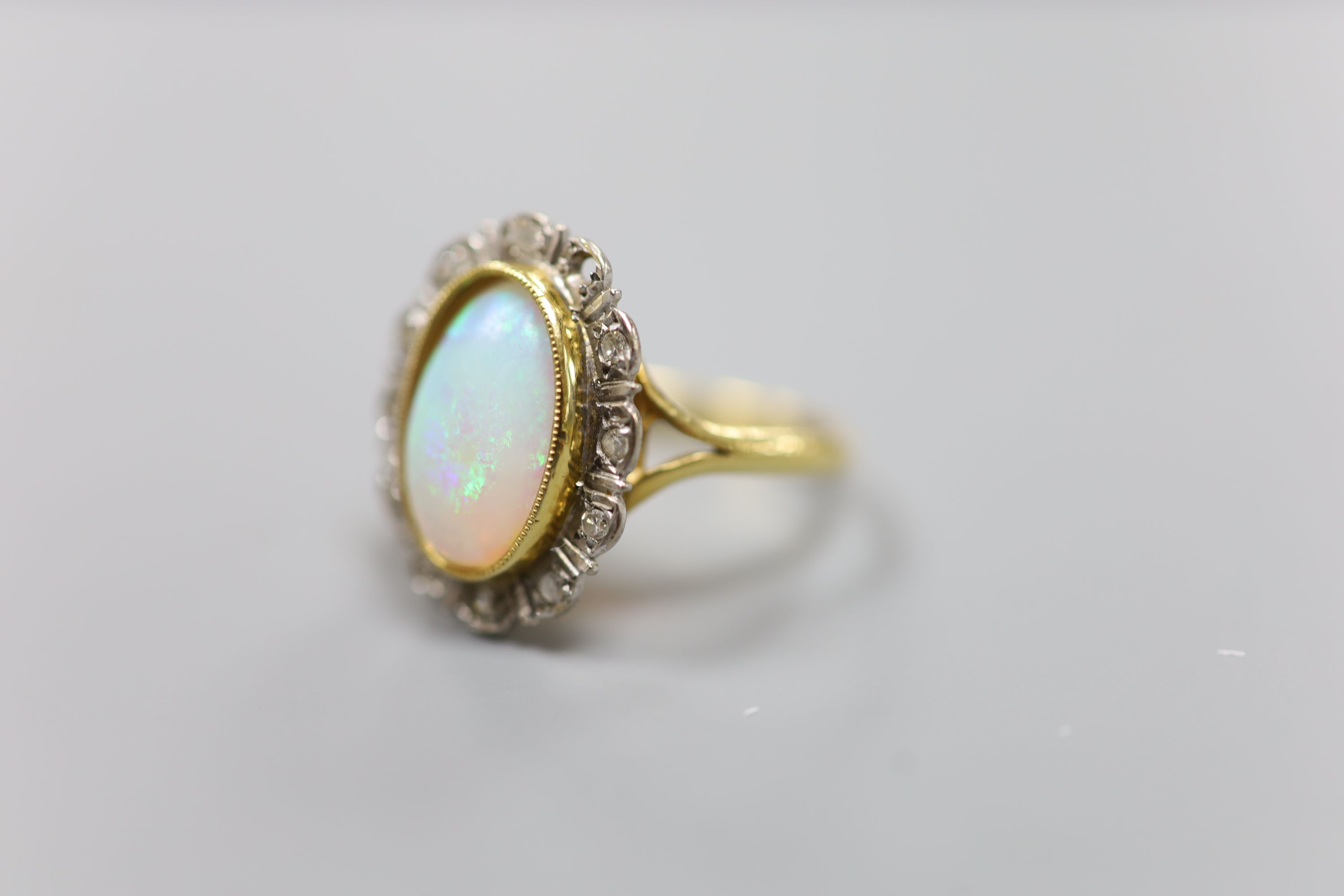 An 18ct, white opal and illusion set diamond oval cluster ring (one diamond missing)
